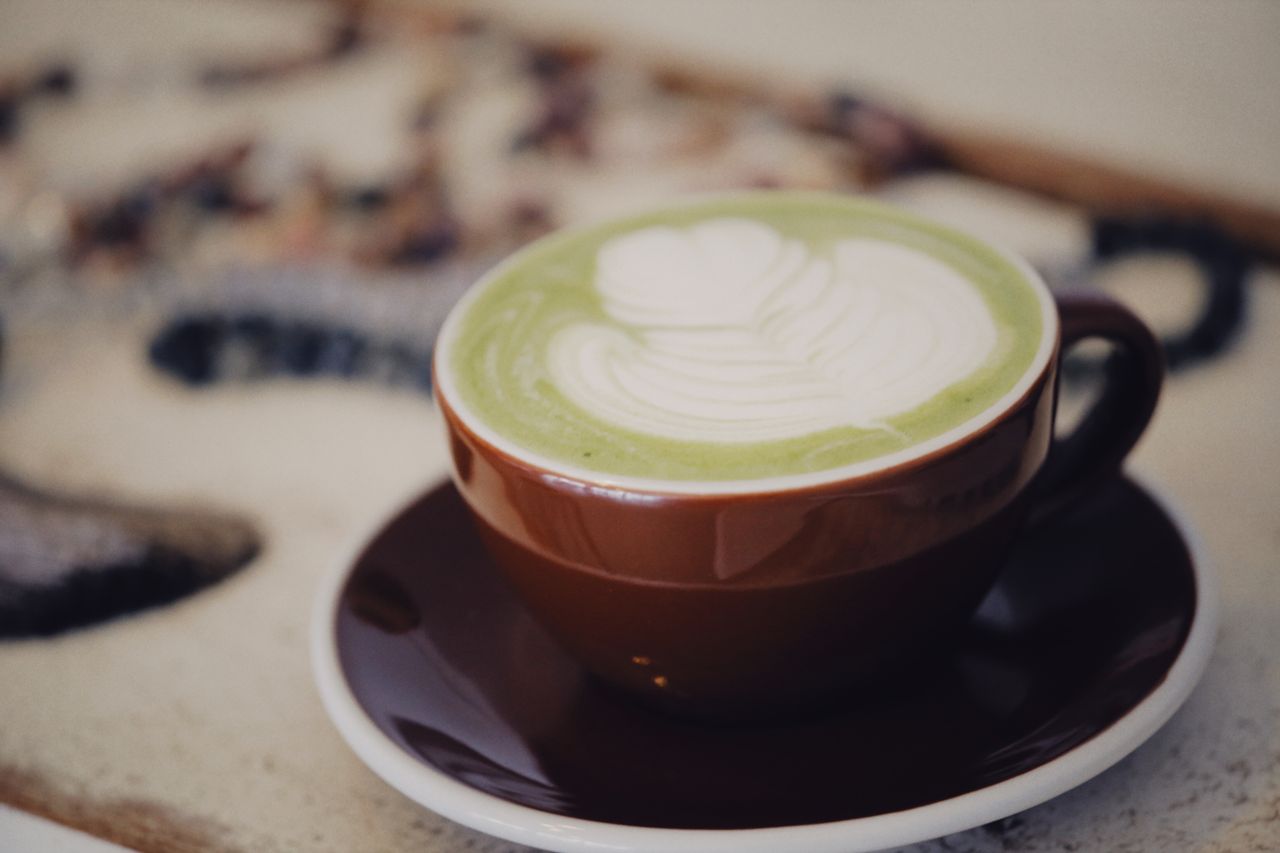 A close-up view of a creamy matcha latte with latte art served in a brown cup.