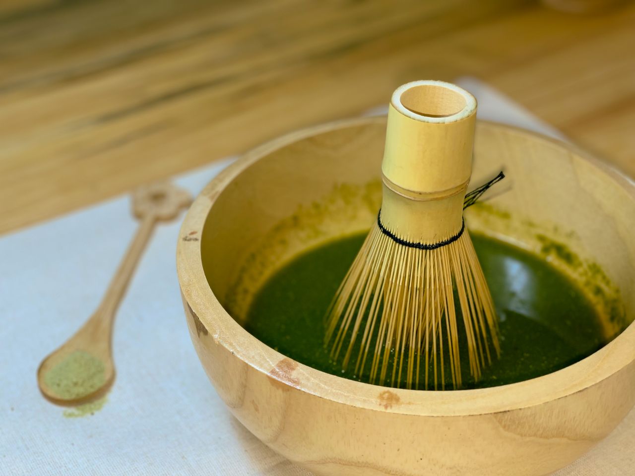 A bamboo whisk in a wooden bowl with matcha tea on a wooden surface.