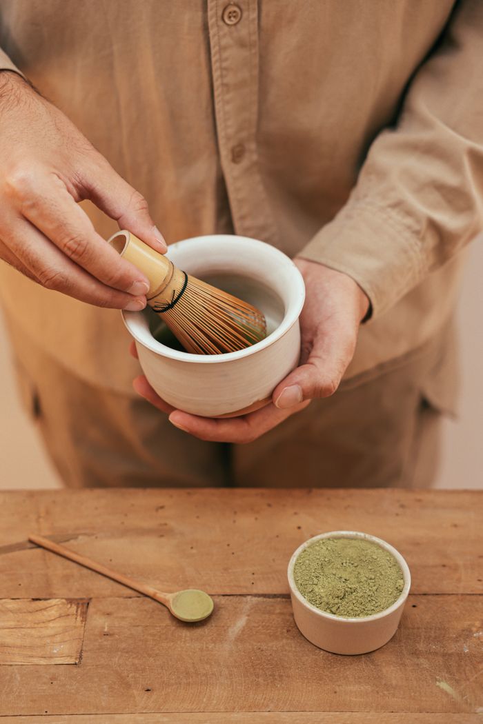 Hand preparing matcha with a bamboo whisk, creating an authentic tea experience.