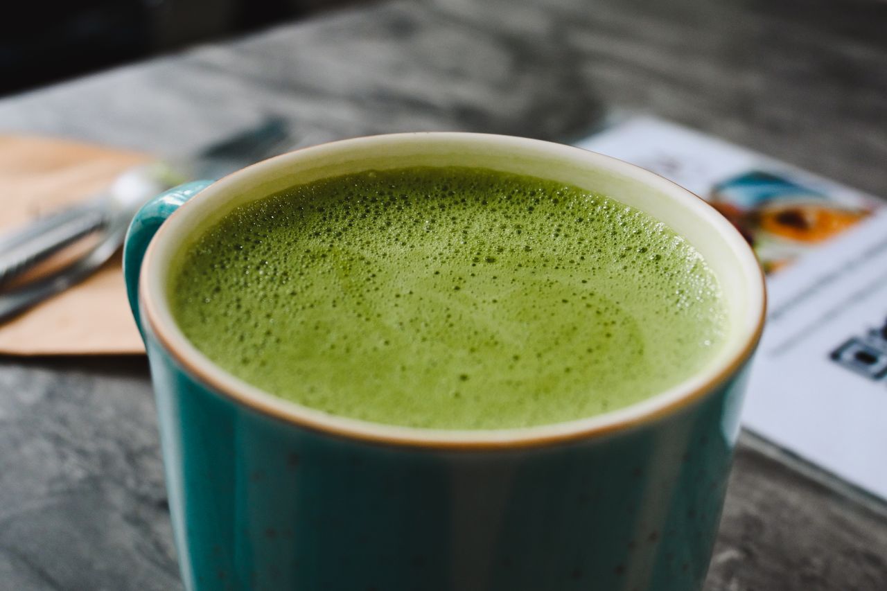 Close-up of a hot matcha latte with frothy green tea in a blue ceramic cup.